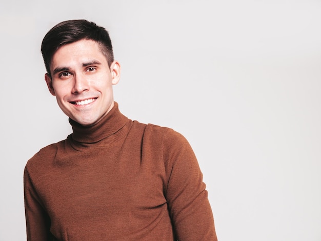 Portrait of handsome smiling model Sexy stylish man dressed in brown turtleneck sweater and jeans Fashion hipster male posing in studio