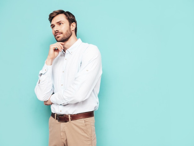 Portrait of handsome smiling model Sexy stylish man dressed in shirt and trousers Fashion hipster male posing near blue wall in studio Isolated