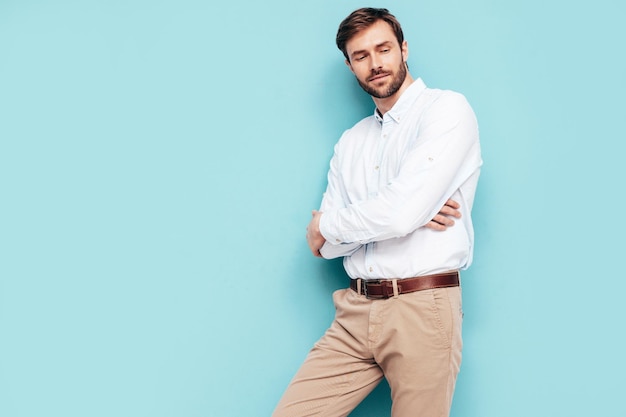 Portrait of handsome smiling model Sexy stylish man dressed in shirt and trousers Fashion hipster male posing near blue wall in studio Isolated