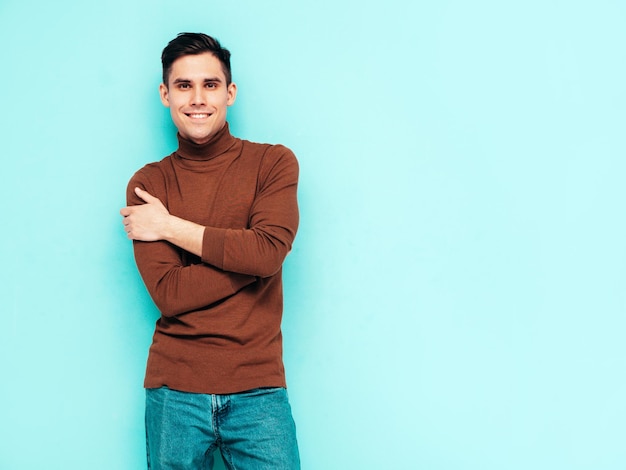 Portrait of handsome smiling model Sexy stylish man dressed in turtleneck sweater and jeans Fashion hipster male posing on grey background in studio Isolated