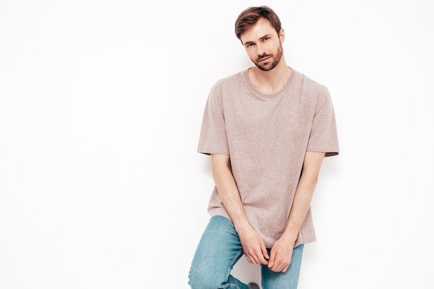 Portrait of handsome smiling stylish hipster lambersexual model Sexy man dressed in pink Tshirt and jeans Fashion male isolated on white wall in studio