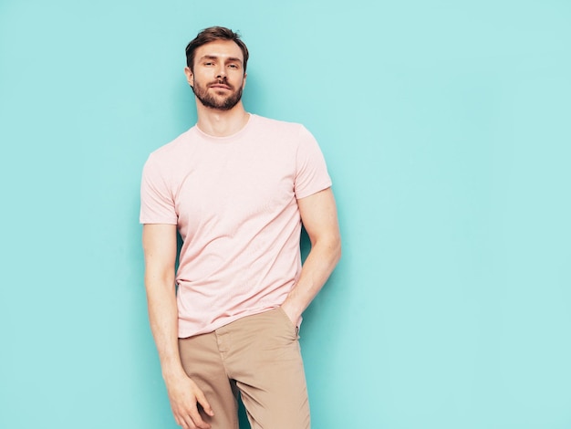 Ritratto di modello lambersexual bello sorridente elegante hipster uomo sexy vestito in maglietta rosa e pantaloni moda maschio isolato sulla parete blu in studio Foto Premium