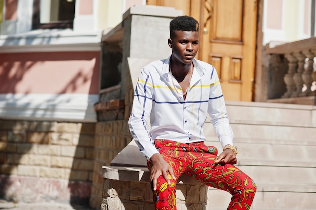 Ritratto di uomo bello ed elegante modello afroamericano in pantaloni rossi e camicia bianca