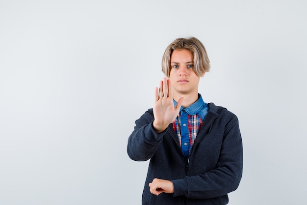 Portrait of handsome teen boy showing stop gesture in shirt, hoodie and looking reluctant front view