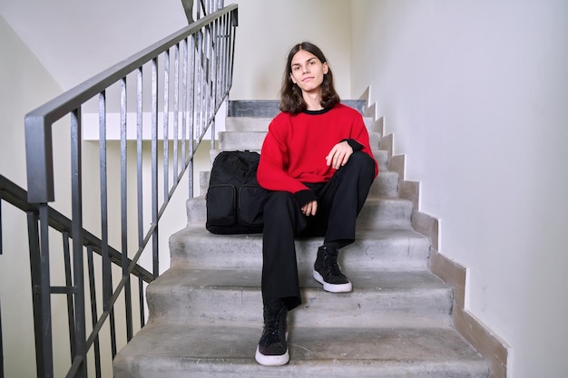 Portrait of a handsome teenage male 17 18 years old sitting on the stairs Smiling trendy guy student with a backpack Youth lifestyle fashion style young people concept