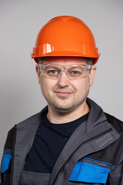 Portrait of a handsome worker builder in overalls helmet and glasses on a white background