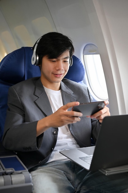 Portrait handsome young asian businessman enjoys playing a\
mobile game during the flight