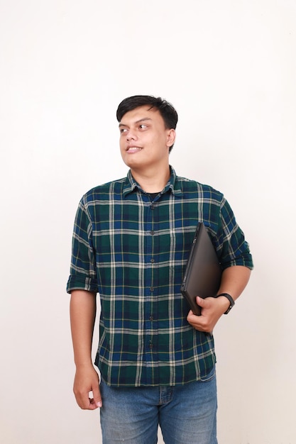 Portrait of handsome young asian college student standing looking sideways while holding a laptop