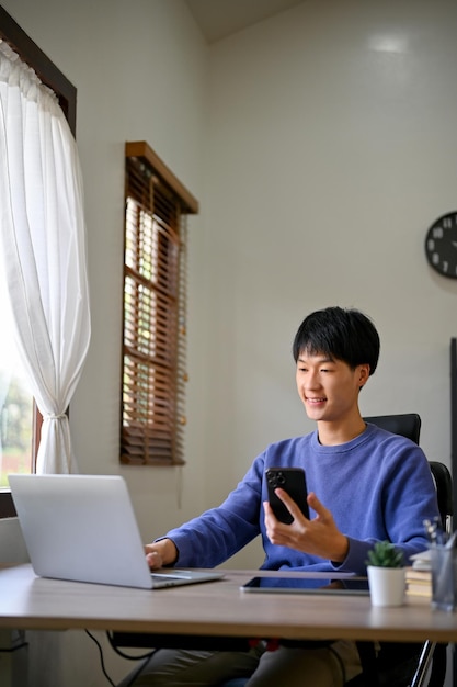 Portrait of handsome young Asian male office worker sits at his desk using laptop