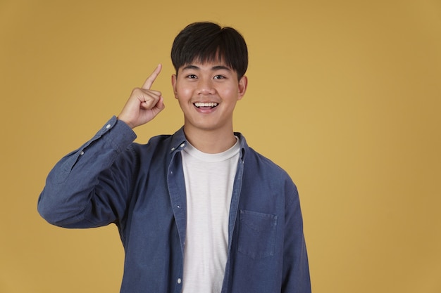 Portrait of handsome young asian man dressed casually smiling pointing finger up having idea isolated