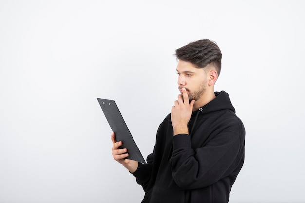 Portrait of handsome young bearded man reading notes on clipboard