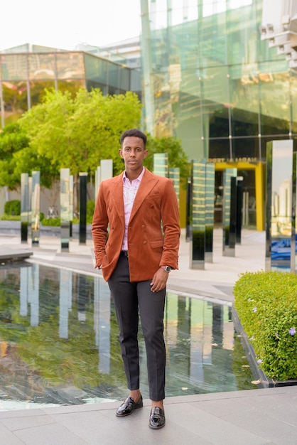 Portrait of handsome young black African businessman standing outdoors in city full length shot