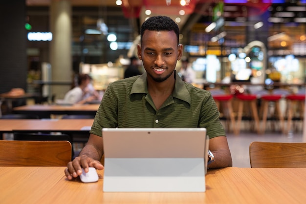 Ritratto di bel giovane uomo di colore che utilizza il computer portatile nella caffetteria