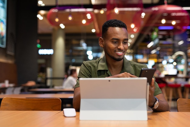 Ritratto di bel giovane uomo di colore che utilizza il computer portatile nella caffetteria