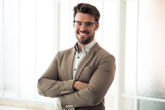 Portrait of handsome young business man looking at camera while standing in the office.