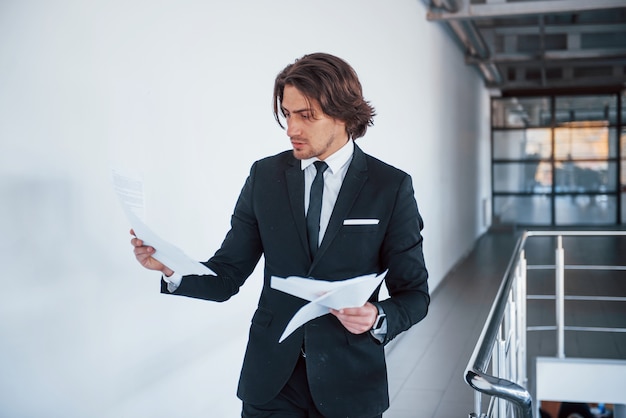 Portrait of handsome young businessman in black suit and tie that reads documents.