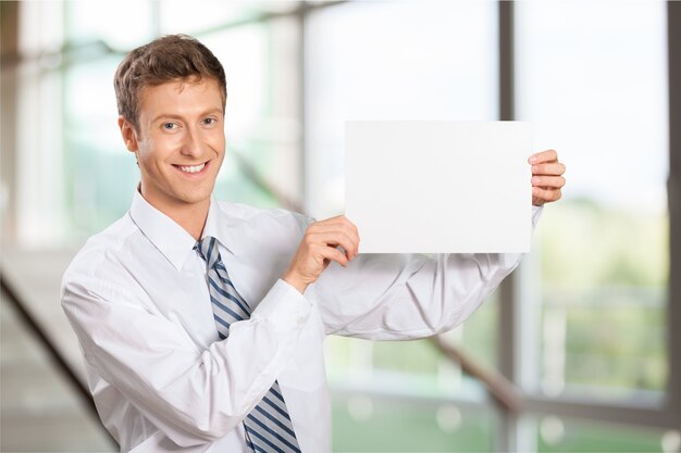 Portrait of handsome young businessman holding blank banner and looking at camera at office