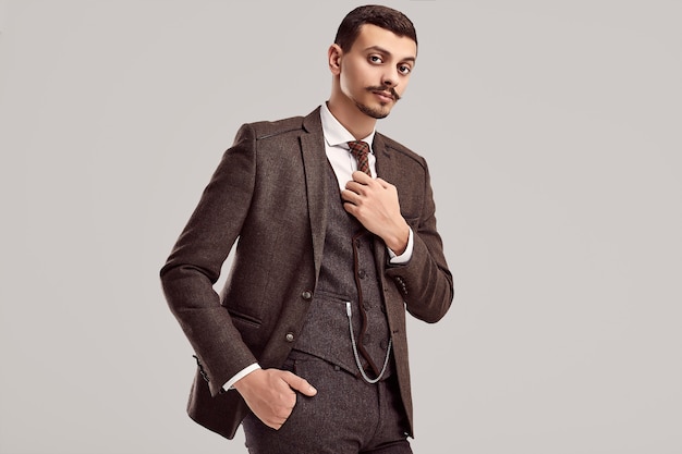 Portrait of handsome young confident arabic businessman with fancy mustache in woolen brown full suit on studio background