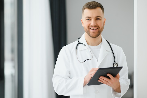 Foto ritratto di bel giovane medico sul corridoio dell'ospedale guardando la fotocamera, sorridente.