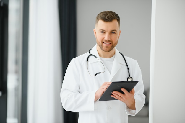 Ritratto di bel giovane medico sul corridoio dell'ospedale guardando la fotocamera sorridente