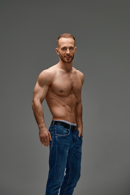 Portrait of a handsome young guy model a shirtless with a muscular healthy body showing off his biceps muscles on a gray background