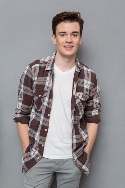 Portrait of handsome young happy positive man in checkered shirt  posing and smiling on gray wall