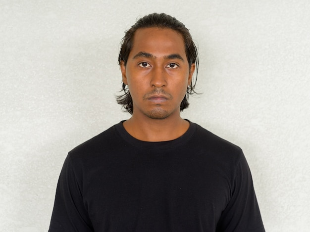 Portrait of handsome young Indian man against plain background