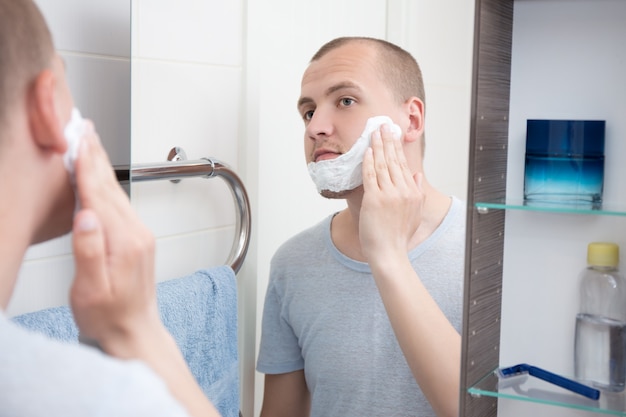 Ritratto di un bel giovane che si applica la crema da barba sul viso