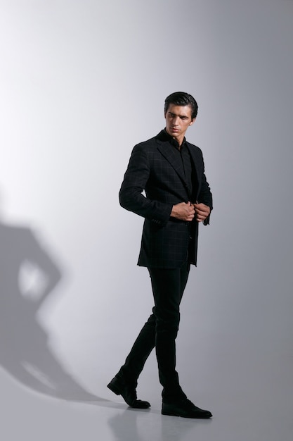 Portrait of handsome young man in black stylish suit, isolated on white background. Full length image.