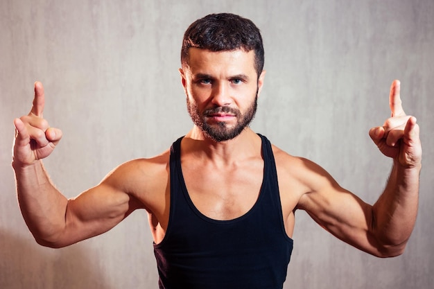 Portrait of a handsome young man in a black Tshirt on a gray background sports man smiling and flirting