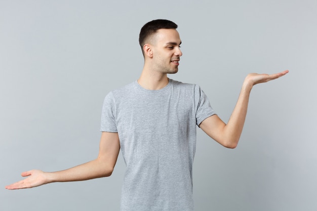 Portrait of handsome young man in casual clothes spreading, looking and pointing hands aside 