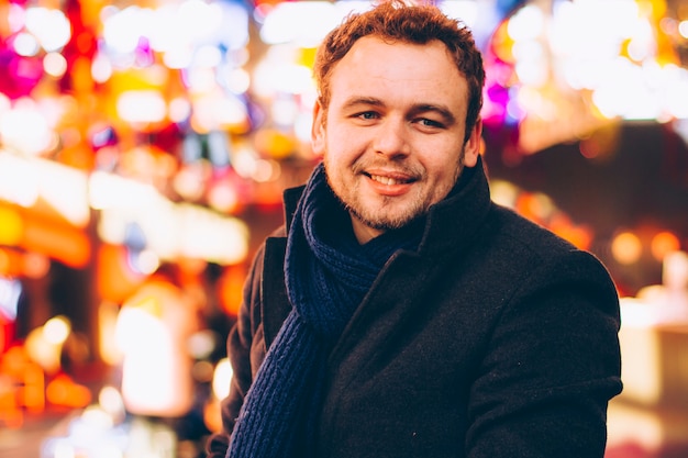 Portrait of a handsome young man in a coat in a night city in the light of lights