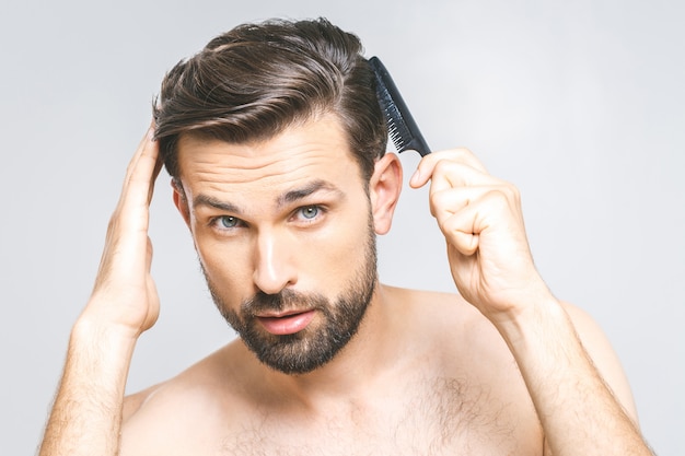 Portrait of handsome young man combing his hair in bathroom. Isolated over grey background.