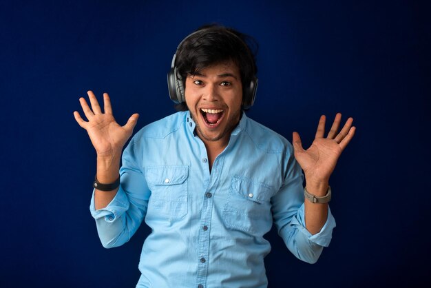 Portrait of a handsome young man enjoying music on headphones on blue background.