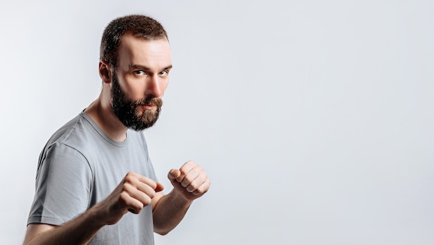 Portrait of handsome young man frowning while looking at camera holding fists and boxing on white background with space for advertisement mock up