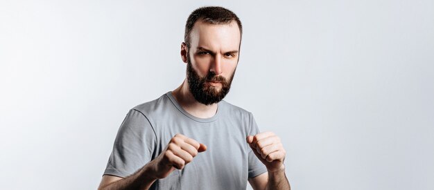 Ritratto di un bel giovane accigliato mentre guarda la telecamera tenendo i pugni e la boxe su sfondo bianco con spazio per la pubblicità mock up