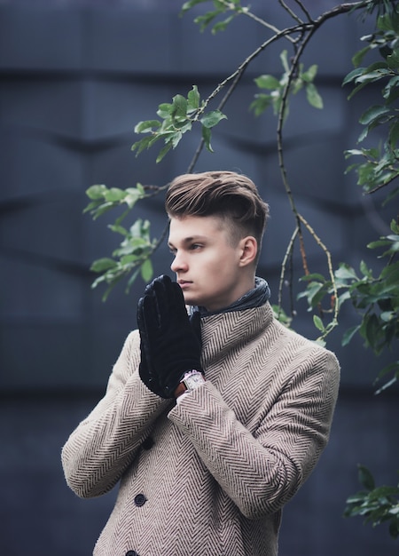 Portrait of a handsome young man in gloves standing on a city street