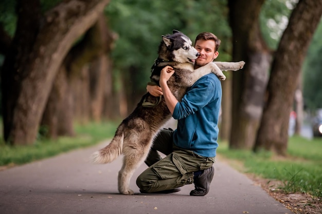 Portrait of a handsome young man and his beloved dog Siberian Husky hugging in nature