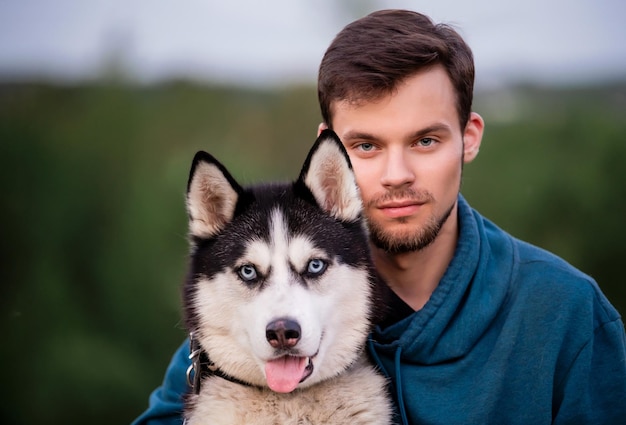 Photo portrait of a handsome young man and his pet dog siberian husky in nature