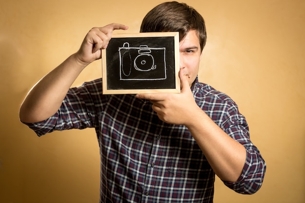 Portrait of handsome young man holding camera drawn on small blackboard