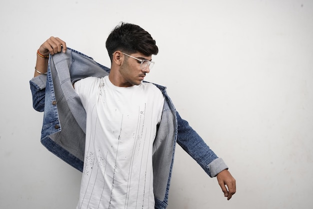 Portrait of handsome young man holding his denim jacket while standing on light plane background