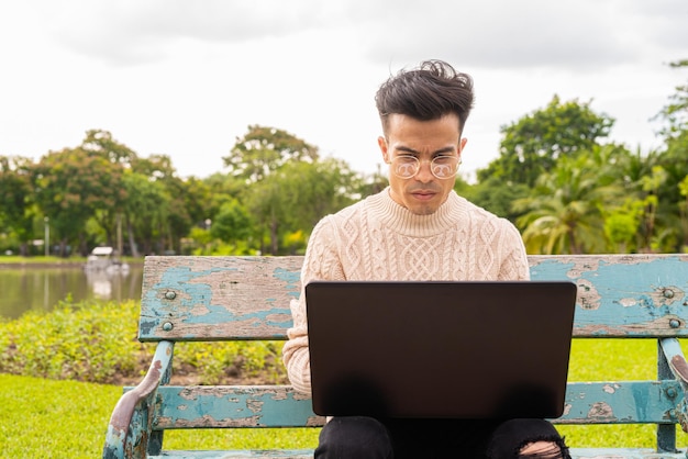 Ritratto di bel giovane nel parco durante l'estate utilizzando il computer portatile