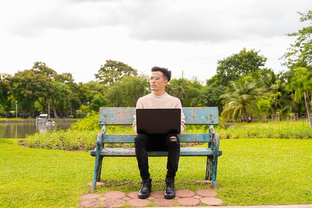 ラップトップコンピューターを使用して夏の間に公園でハンサムな若い男の肖像画