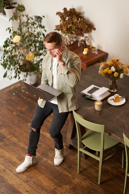 Photo portrait of handsome young man sits with laptop looks at screen with concentrated thoughtful face