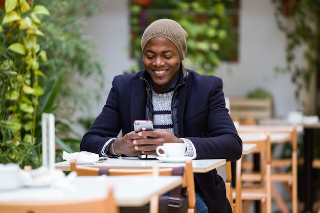 カフェで彼の携帯電話を使用してハンサムな若い男の肖像画。