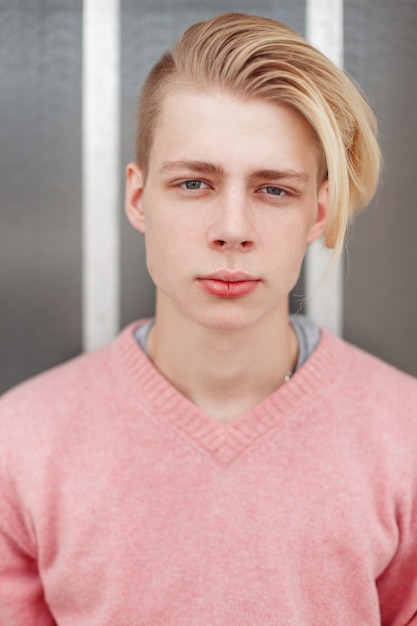 Portrait of a handsome young man with a blond hairstyle in a pink sweater near the wall