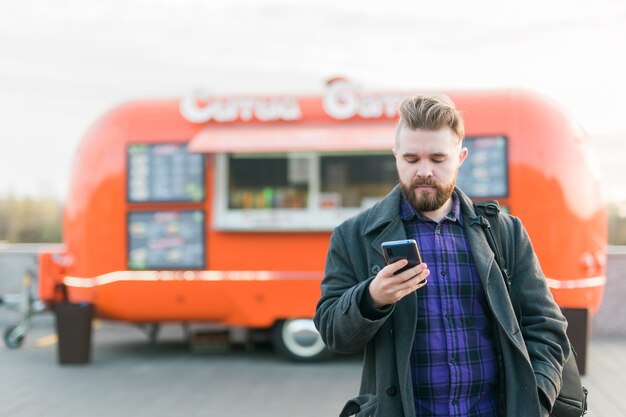 フードトラックの前に立っているスマートフォンを持つハンサムな若い男の肖像画