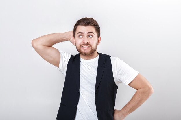 Portrait of handsome young pensive brunette man in white shirt on gray background. guy thinks