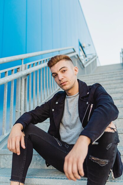 Portrait of a handsome young and rocker man sitting on stairs in the street