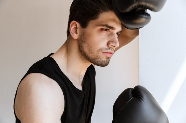 Portrait of a handsome young sports man boxer in gloves standing near window.
